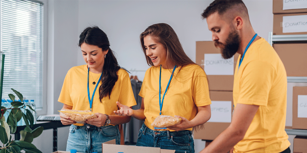 Two women and a man in yellow shirts wearing lanyards for a volunteer project.